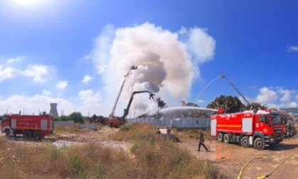 Hills of junk made of car parts, metal and wood are burning. Water cannons shoot at the fire to extinguish and cool the fire.