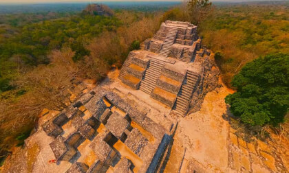 Drone flyover of ancient Maya and Mexica pyramids in a dense jungle, cinematic view, 16K resolution, 60fps, ultra-detailed, atmospheric lighting